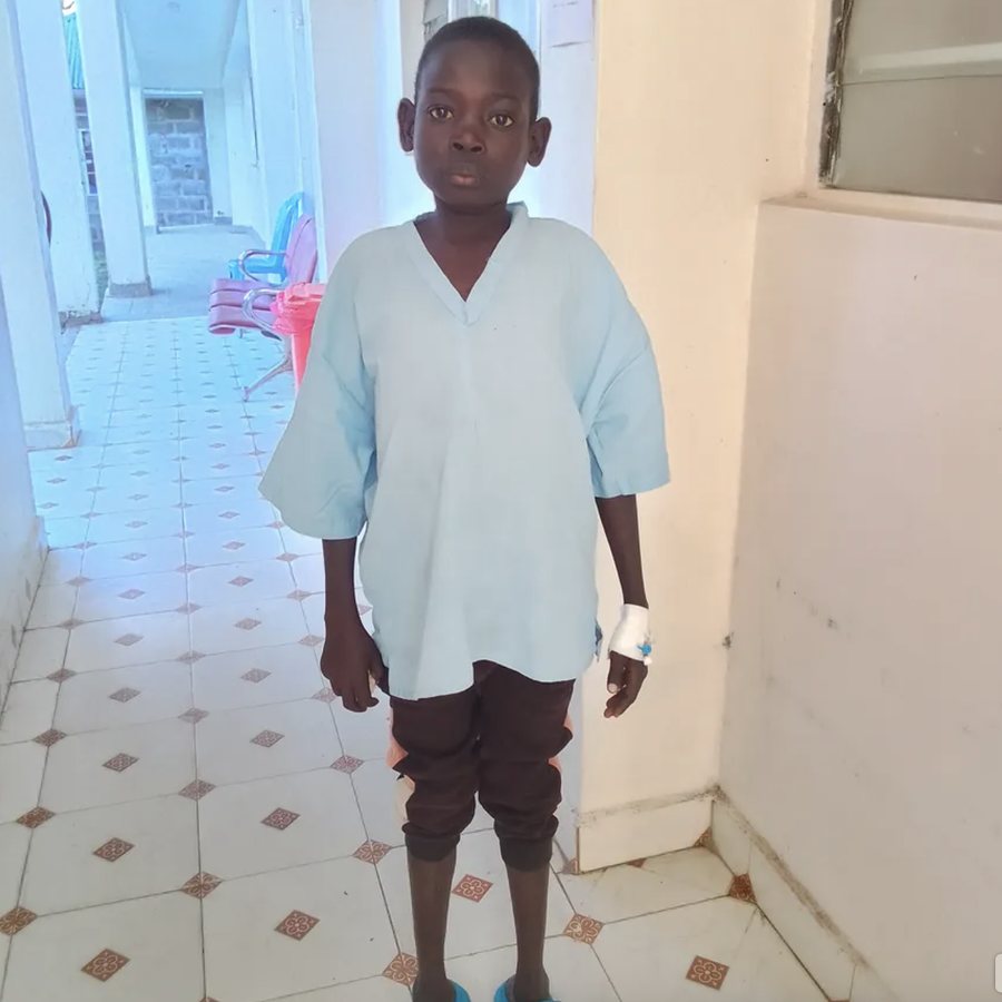 Joseph standing in the hospital corridor in a gown, with a bandaged cannula on his left hand